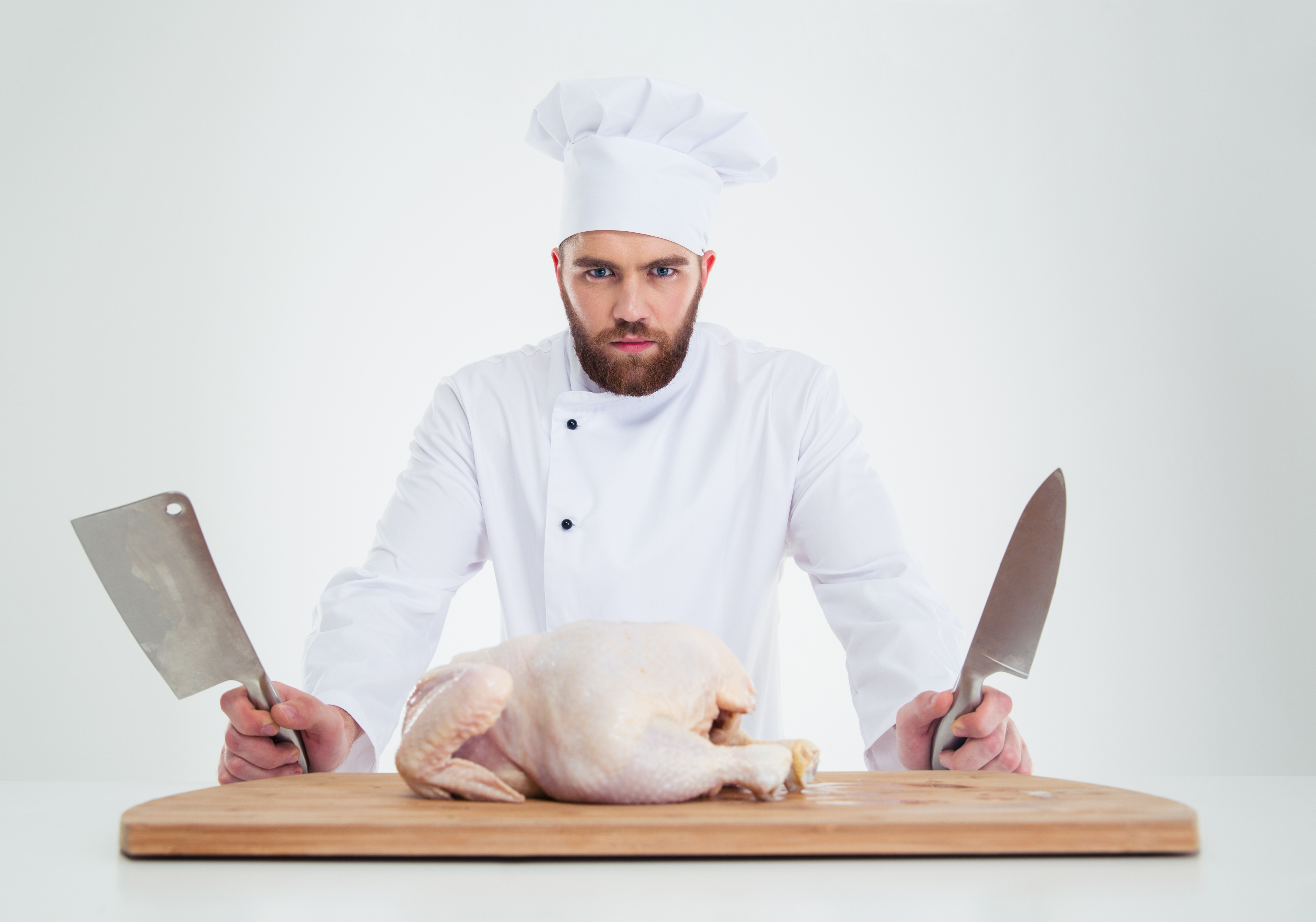 Portrait of a serious male chef cook standing with knifes and chicken 